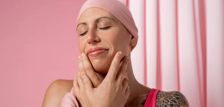 Mulher tocando o próprio rosto e sorrindo, com um lenço rosa na cabeça